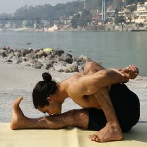 A practitioner in a seated forward fold beside a river