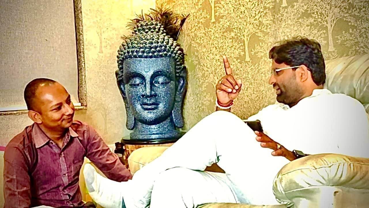 Dr. D.P. Shukla speaking with a visitor beside a blue Buddha head