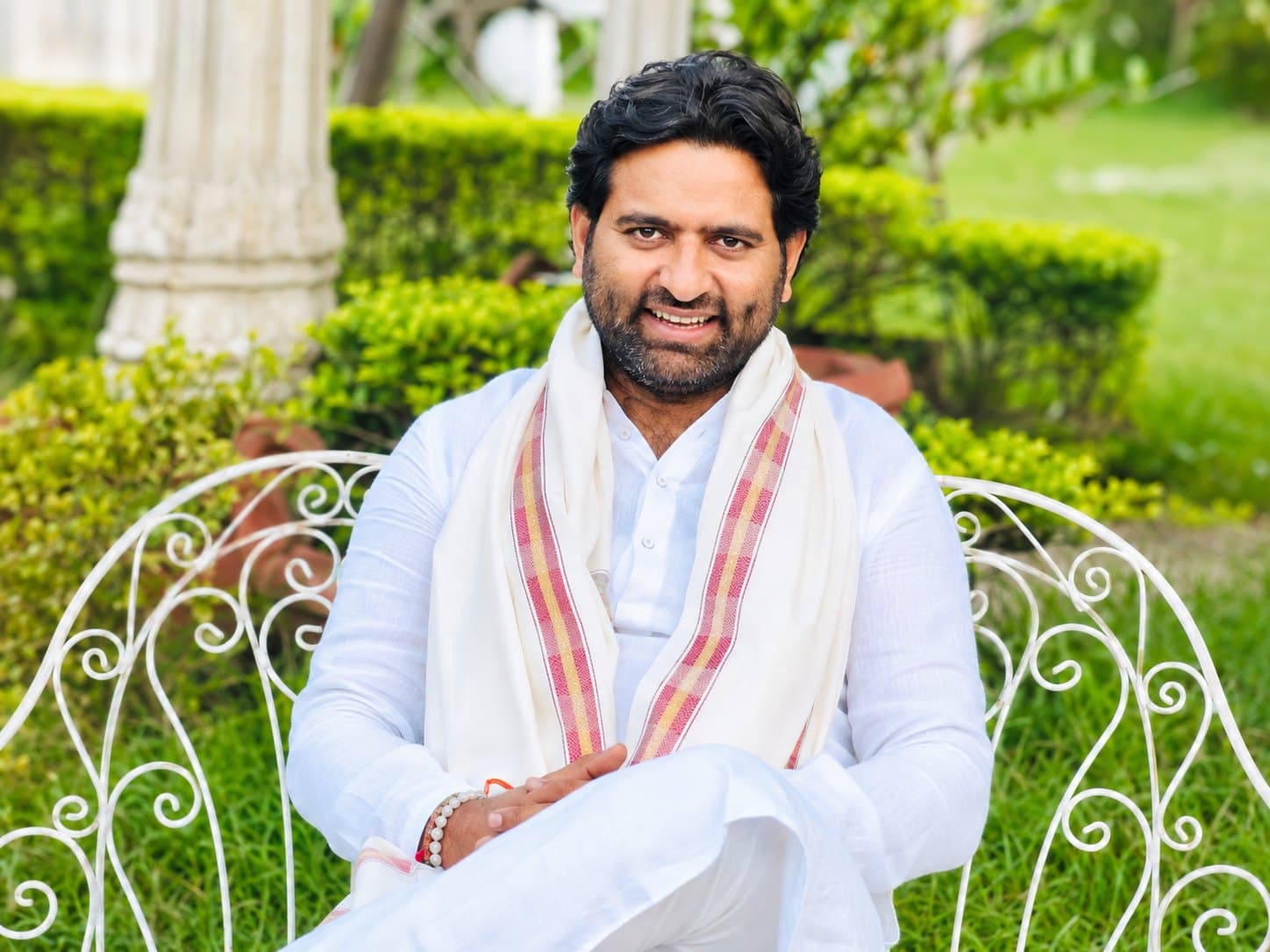 Dr. D.P. Shukla seated in a garden, dressed in white with a shawl, smiling