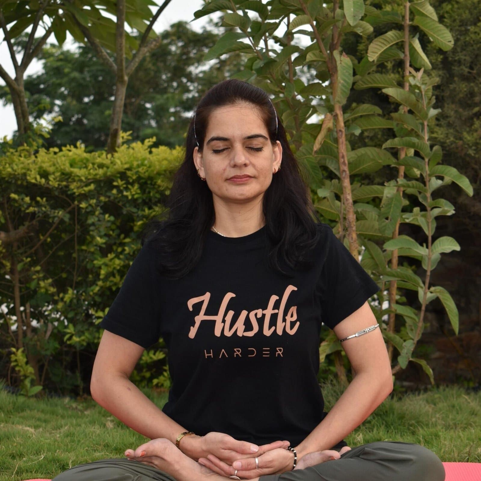 A woman meditating cross-legged in a garden