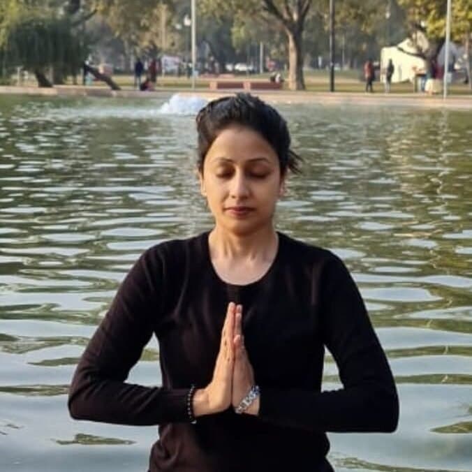 A woman with joined palms meditating beside a lake