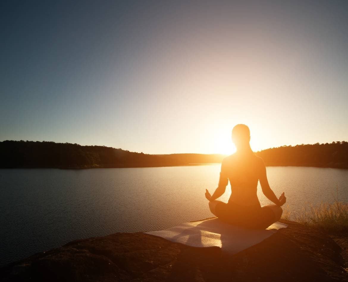 Silhouette of a person meditating on a rock by the water at sunrise